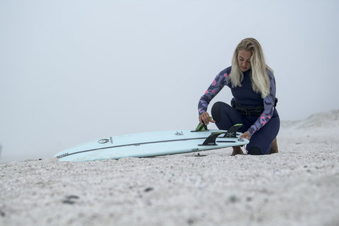 ION Amaze Amp 5/4mm Backzip-Fullsuit in dunkelblau mit pinkem Print beim Wellenreiten am Strand