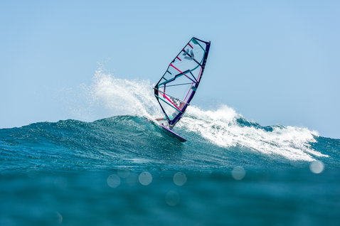 Voile de windsurf freestyle Duotone Super Hero HD pendant le surf de vagues sur l'océan en bleu sarcelle, marine et rose