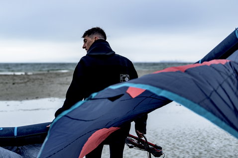 ION Neo Shelter Jacket Core veste néoprène homme en bleu marine sombre lors d'une session kitesurf sur la plage