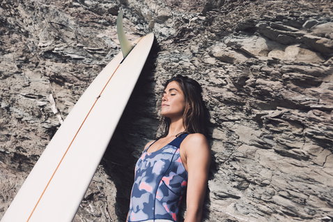 ION Amaze Shorty Crossback 1.5mm shorty wetsuit in navy, pink and coral during surfing at rocky cliffs