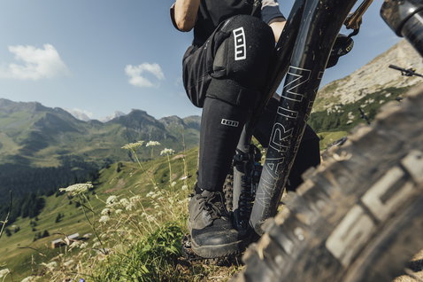 ION Bike S-Sleeve Amp shin pad in black during mountain biking on an alpine trail