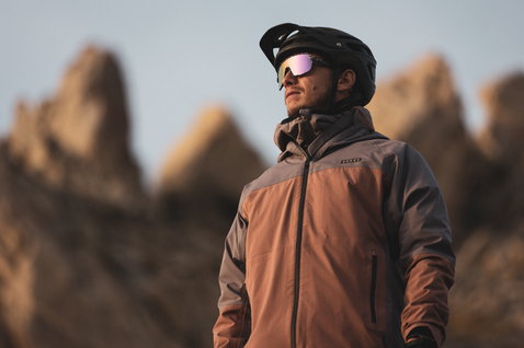 ION Bike Shelter 3L Herren-Fahrradjacke in braun und grau beim Mountainbiken in den Bergen