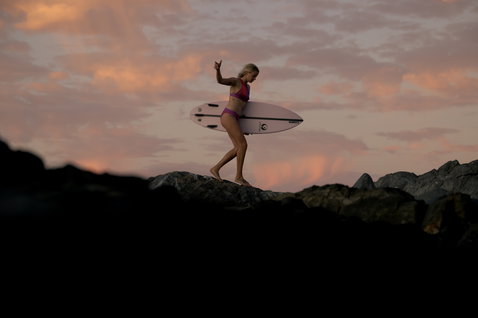 ION SurfKini bikini in magenta during wave surfing on coastal rocks at golden hour