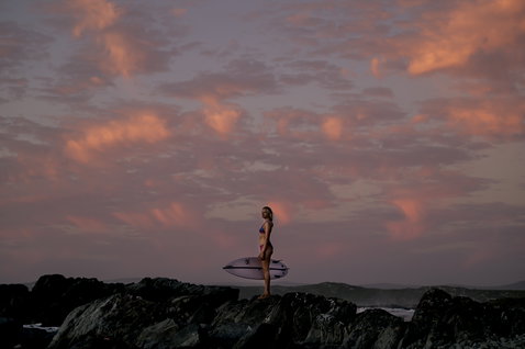 ION Surfkini bikini in dusty rose during wave riding on a rocky coastline at golden hour