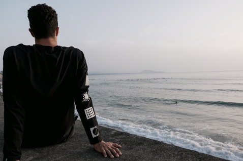 ION Bike Vibes long-sleeve tee men in black with graphic sleeve prints seated at the coast