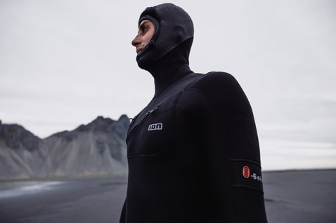 ION Seek Select 6/5mm Kapuzen-Neoprenanzug mit Frontverschluss in schwarz beim Surfen an felsiger Küste