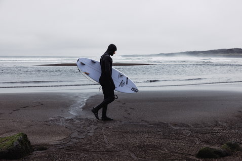 ION Seek Select 6/5mm Kapuzen-Frontzip-Neoprenanzug in schwarz beim Wellenreiten am Strand