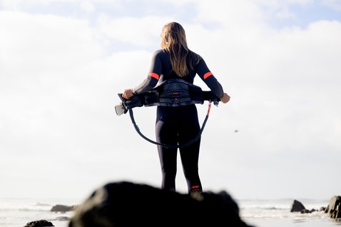 ION Amaze Amp 4/3mm front-zip fullsuit in black and coral during kitesurfing at the coast