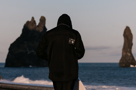 ION Neo Shelter Jacket Core uomo giacca in neoprene in nero indossata su una costa rocciosa