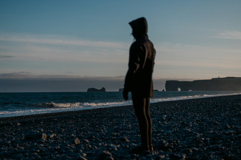 ION Neo Shelter Jacket Core giacca in neoprene da uomo in nero su una spiaggia rocciosa al tramonto