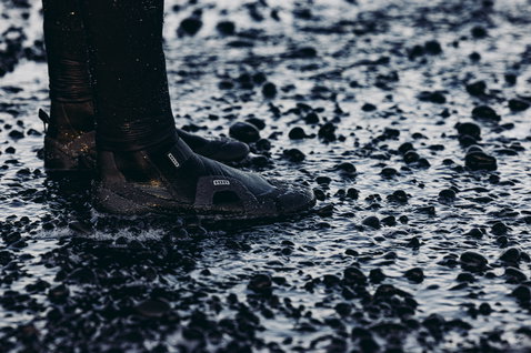 ION Ballistic Boots 3/2 neoprene split-toe boots in black during kitesurfing on a rocky shore