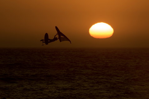 ION Slash Amp helmet during kitesurfing — rider silhouette performing an aerial trick over the ocean at sunset