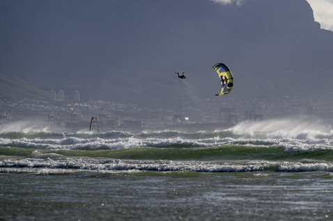 ION Seek Amp 4/3mm back-zip fullsuit wetsuit during kitesurfing on the ocean with mountain backdrop