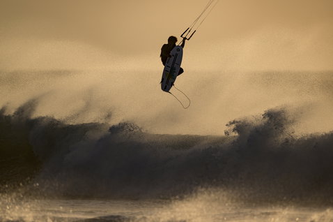 ION Seek Amp 4/3mm back-zip fullsuit during kitesurfing above breaking waves at golden hour