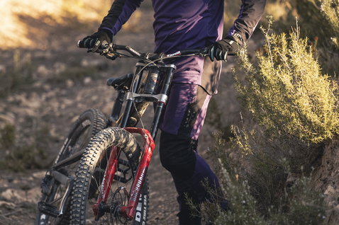 Pantaloni da ciclismo ION Scrub Amp BAT in viola scuro durante freeride su trail di montagna