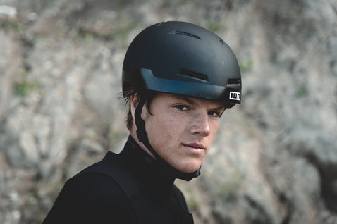 ION Mission Helm in matt schwarz, getragen von einem Athleten an einer Felsküste
