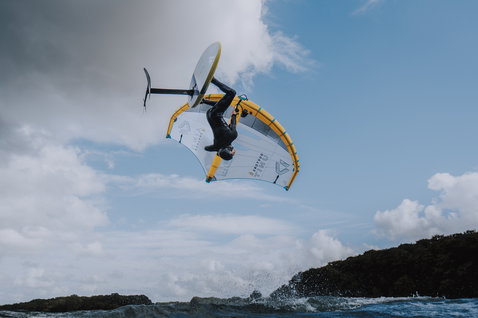 ION Mission Helm beim Wing Foiling über dem Meer mit felsiger Küste im Hintergrund