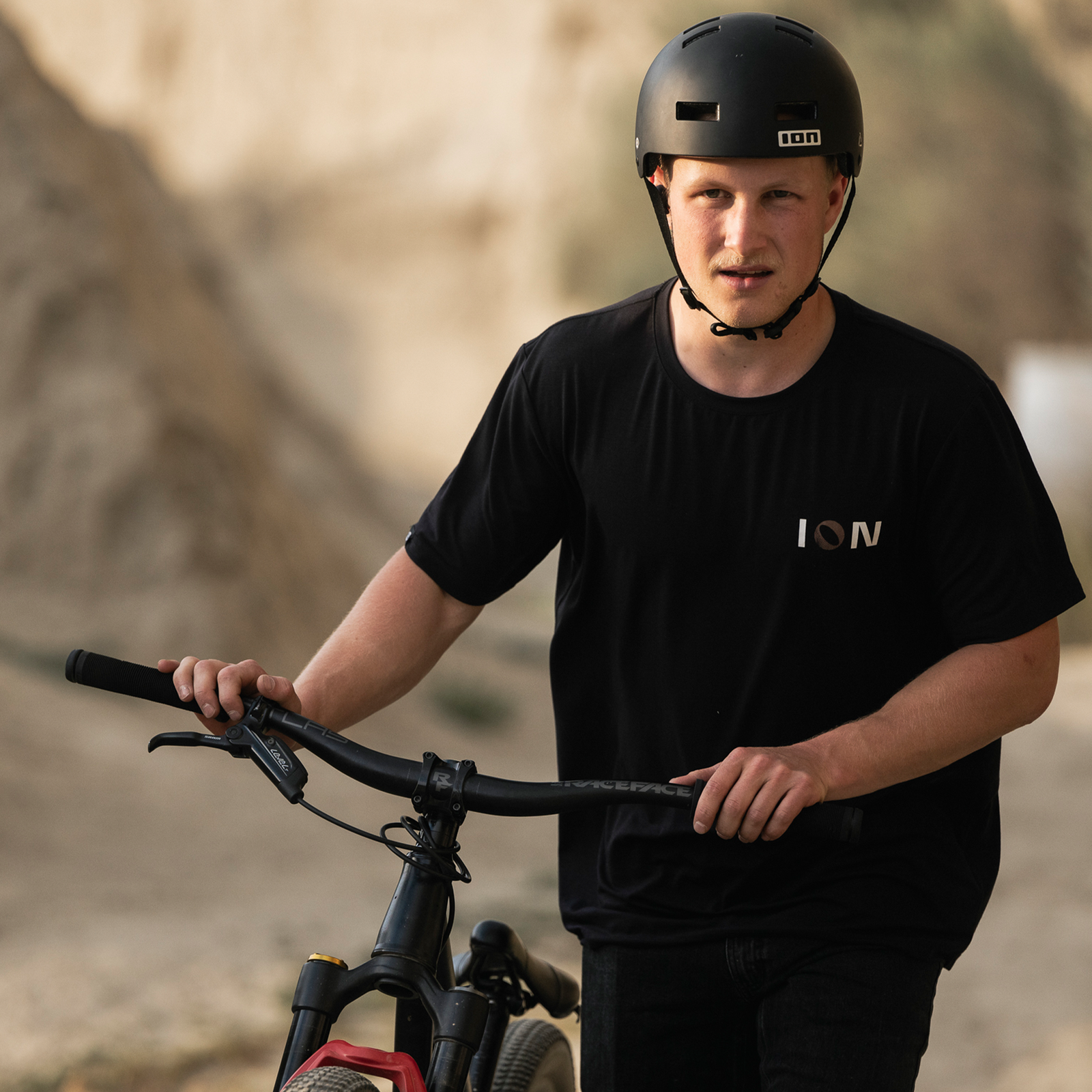 ION Seek bike helmet in matte black worn during mountain biking at a dirt jump park