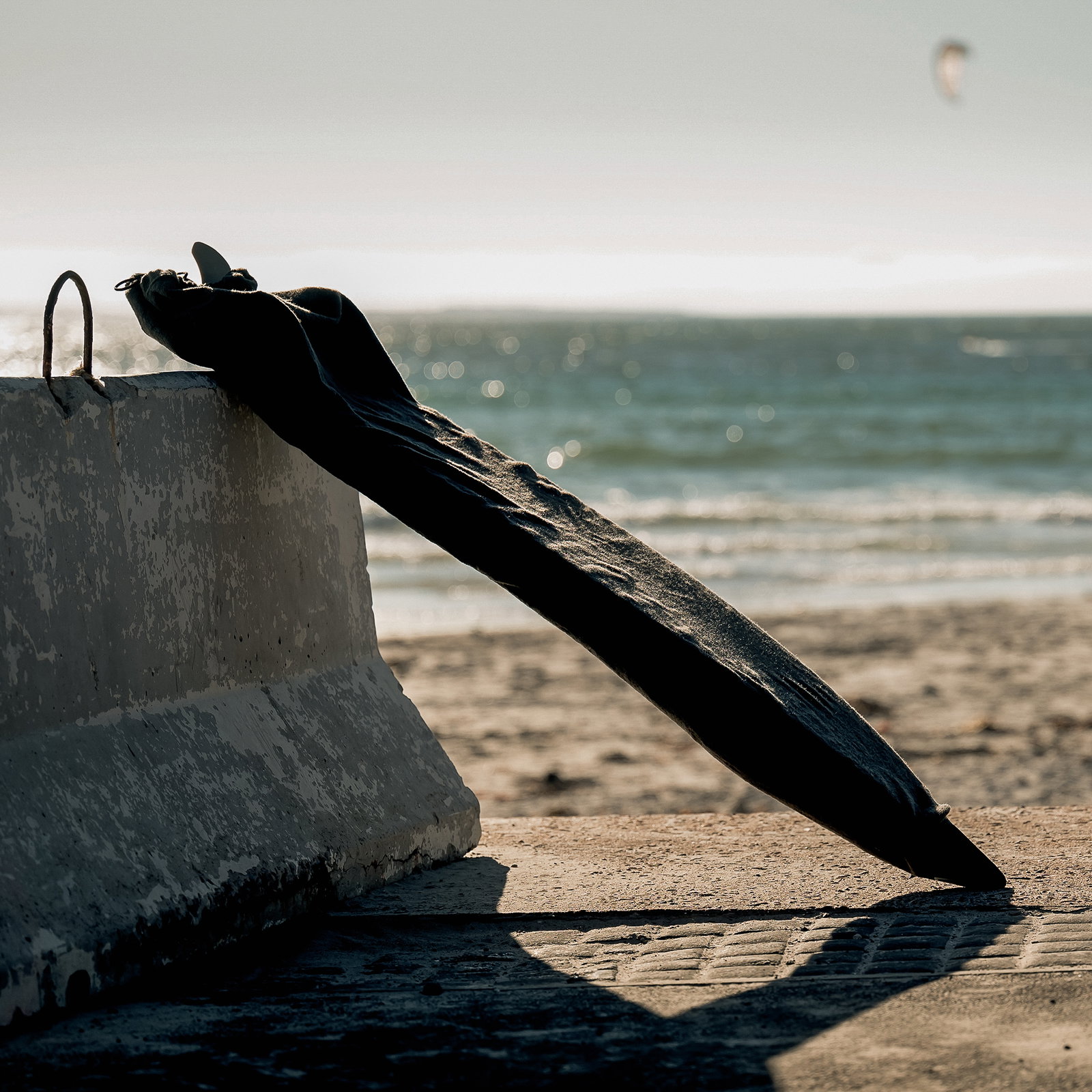 ION Surf Sock board cover 5'9" in black leaning against a concrete wall at the beach