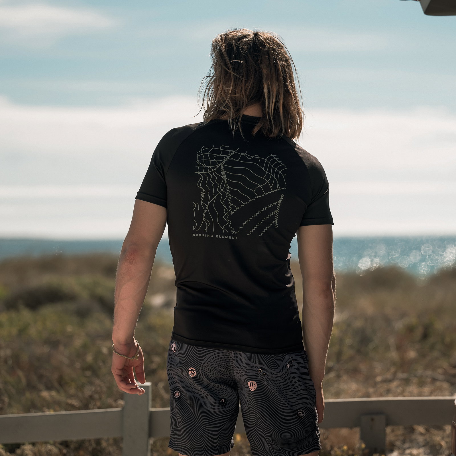 ION Water Rashguard SS men short-sleeve UV top in black with back print worn at the coast