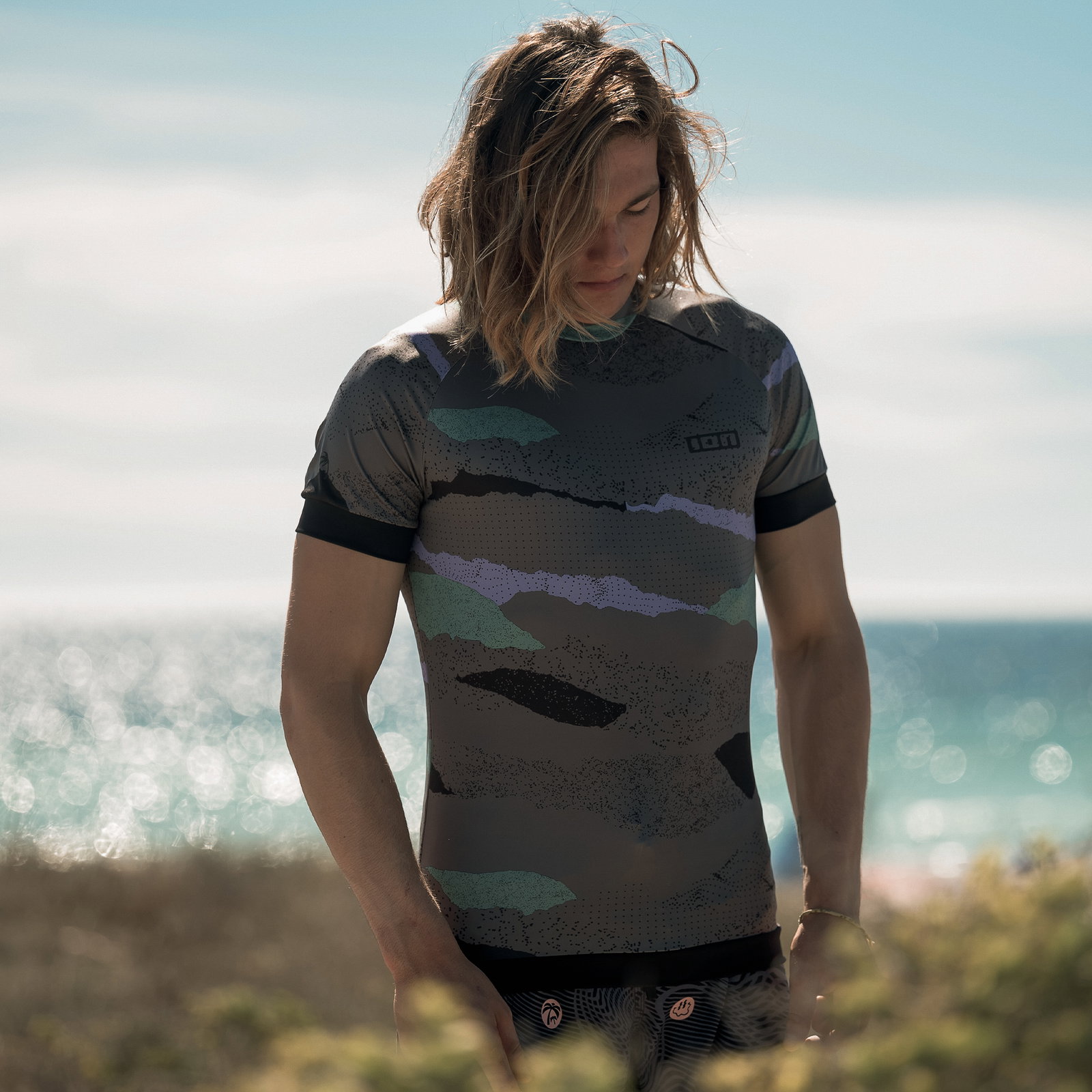 ION Maze Rashguard Kurzarm Herren in dunkelgrau mit abstraktem Print beim Wassersport am Meer