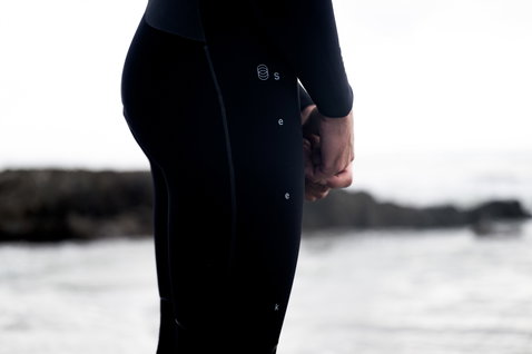 ION Seek Select 5/4mm front-zip fullsuit in black during standing pose at rocky ocean shore