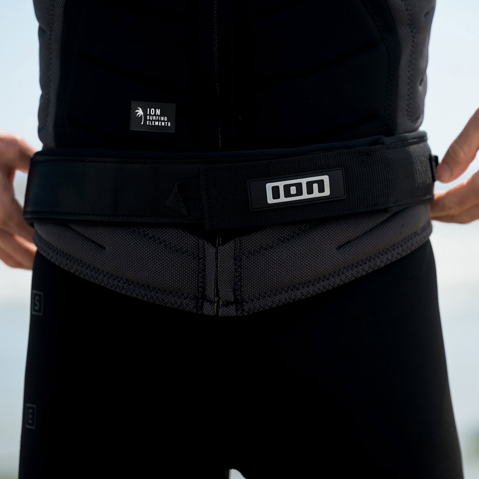 Cinto de anca ION Wing Board Leash Coiled Hip Release em preto usado na cintura em ambiente costeiro