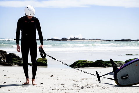 ION Hip Belt durante il wing foiling su spiaggia sabbiosa con foilboard e leash a spirale