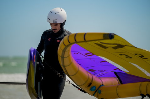 ION Hip Belt durante il wing foiling in spiaggia con atleta in muta ION nera e casco bianco