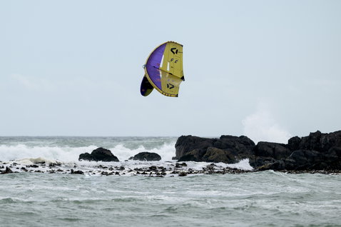 Duotone LEI kite 9,5 m in giallo-verde e viola durante il kitesurf su una costa rocciosa