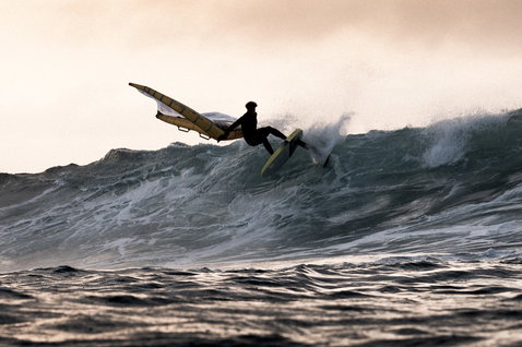 ION Wing Leash Core Coiled Ankle durante il wing foiling sull'oceano tra le onde