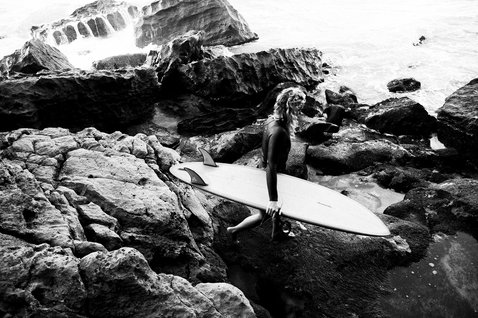 ION Neo Zip Top 2/1 LS Skin top in neoprene donna in nero durante il surf su costa rocciosa