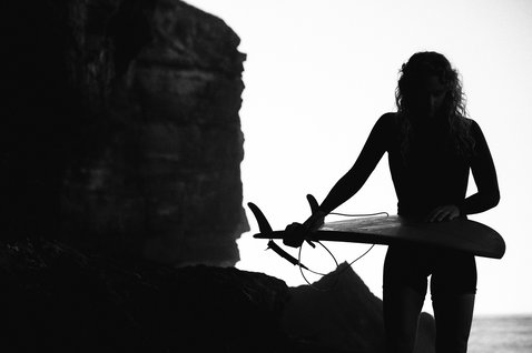 ION Surf Leash Core Ankle during wave surfing at a rocky coastal cliff