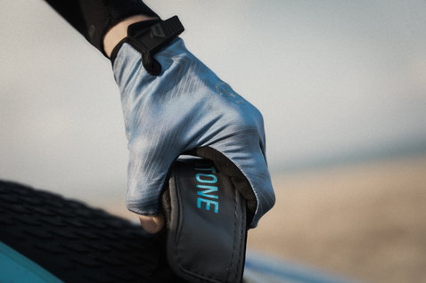 Gants demi-doigts ION Amara en gris foncé et bleu acier lors d'une session de kitesurf en bord de mer