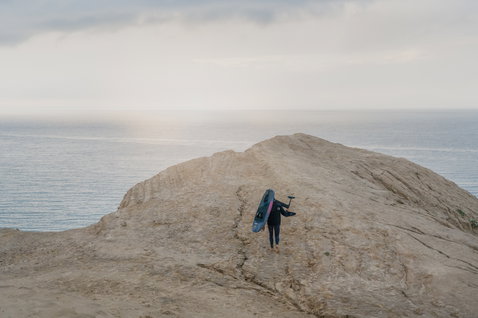ION Neo Hoody Reversible neoprene hoody during wing foiling at a coastal cliff in dark navy