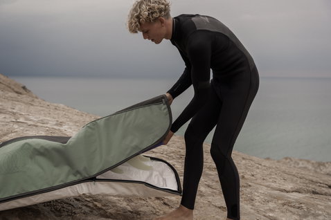 ION Core Stubby windsurf board bag being opened on a rocky beach in charcoal and sage green