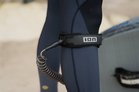 ION Wing Leash Core Coiled Knee leash in black during wing foiling at the beach