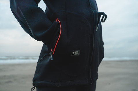 ION Neo Shelter Jacket Amp donna giacca in neoprene 2mm in nero con dettaglio tasca rosso sulla spiaggia