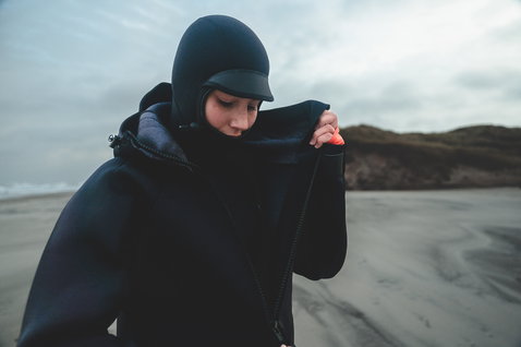 ION Neo Cosy Coat Core manteau en néoprène femme en noir porté sur une plage venteuse avant une session nautique