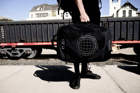 ION Carry-on Wheelie travel bag in black held at a sunny train station