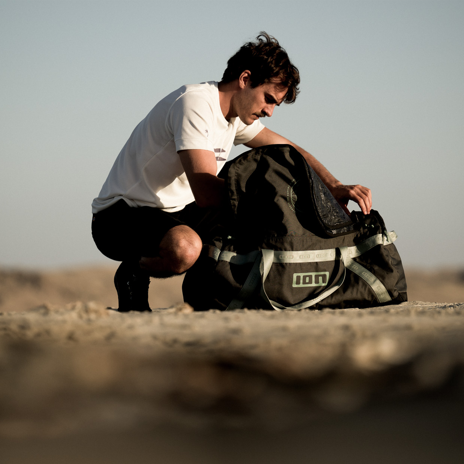 Borsa da viaggio ION Session 90l in marrone scuro-nero durante il packing in spiaggia