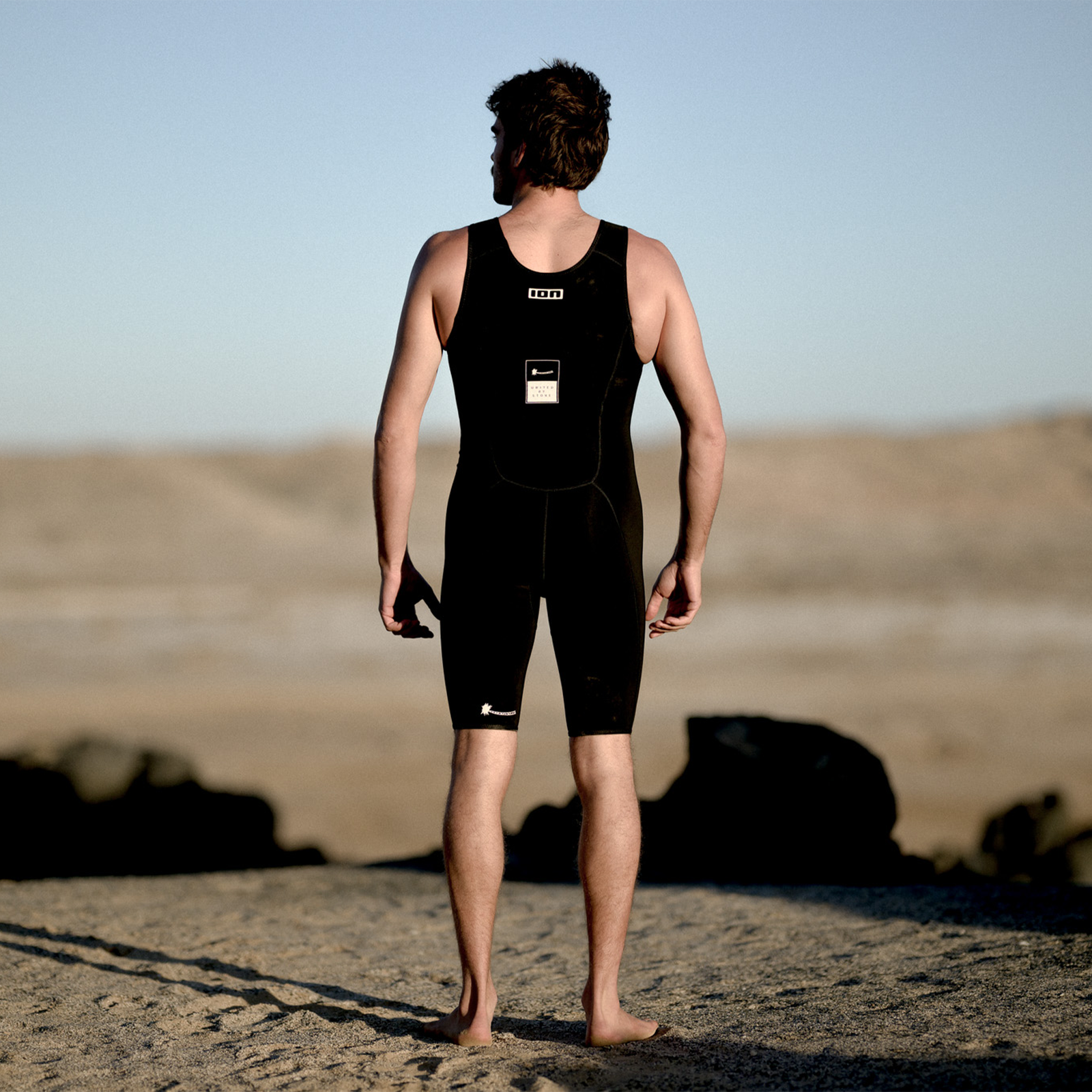 ION Monoshorty 0,5mm Pull-on Shorty in schwarz beim Tragen an einem Sandstrand