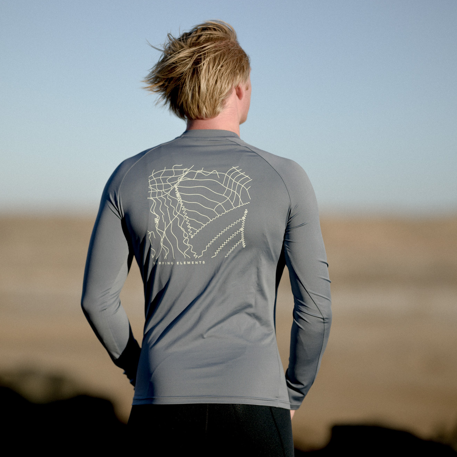 ION Rashguard LS men long-sleeve UV top in dark grey with topo back print worn at the coast
