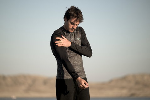 ION Maze rashguard manica lunga uomo in nero con stampa grafica durante sport acquatici in riva al mare