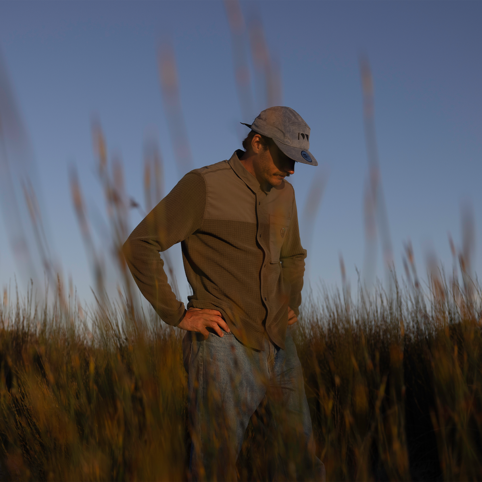Giacca unisex ION Ionic Fleece in marrone oliva indossata all'aperto in un campo alla luce dorata