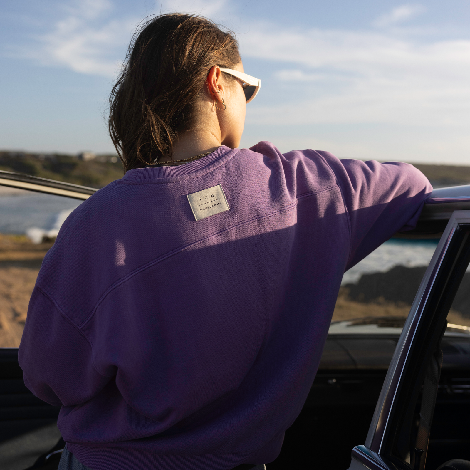 ION Mood women's sweater in purple worn at the coast — back view showing ION woven label