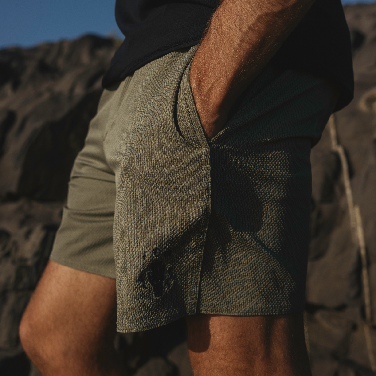 ION Slade Boardshorts 17" Herren in olivgrün mit Mesh-Panel beim Tragen an der Felsküste