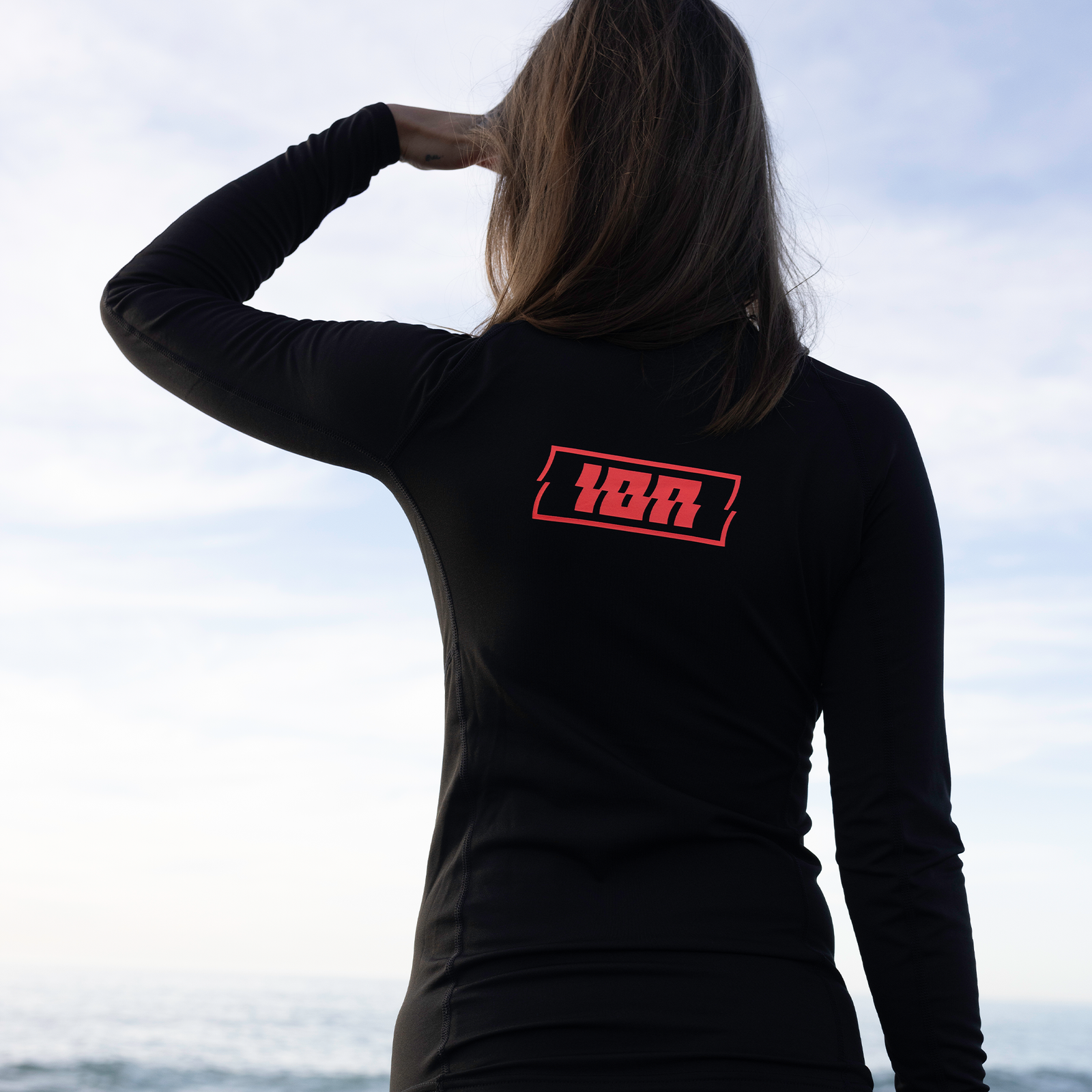ION Water Thermo Top LS Damen Langarm-Thermotop in schwarz mit rotem Logo, Rückenansicht am Meer