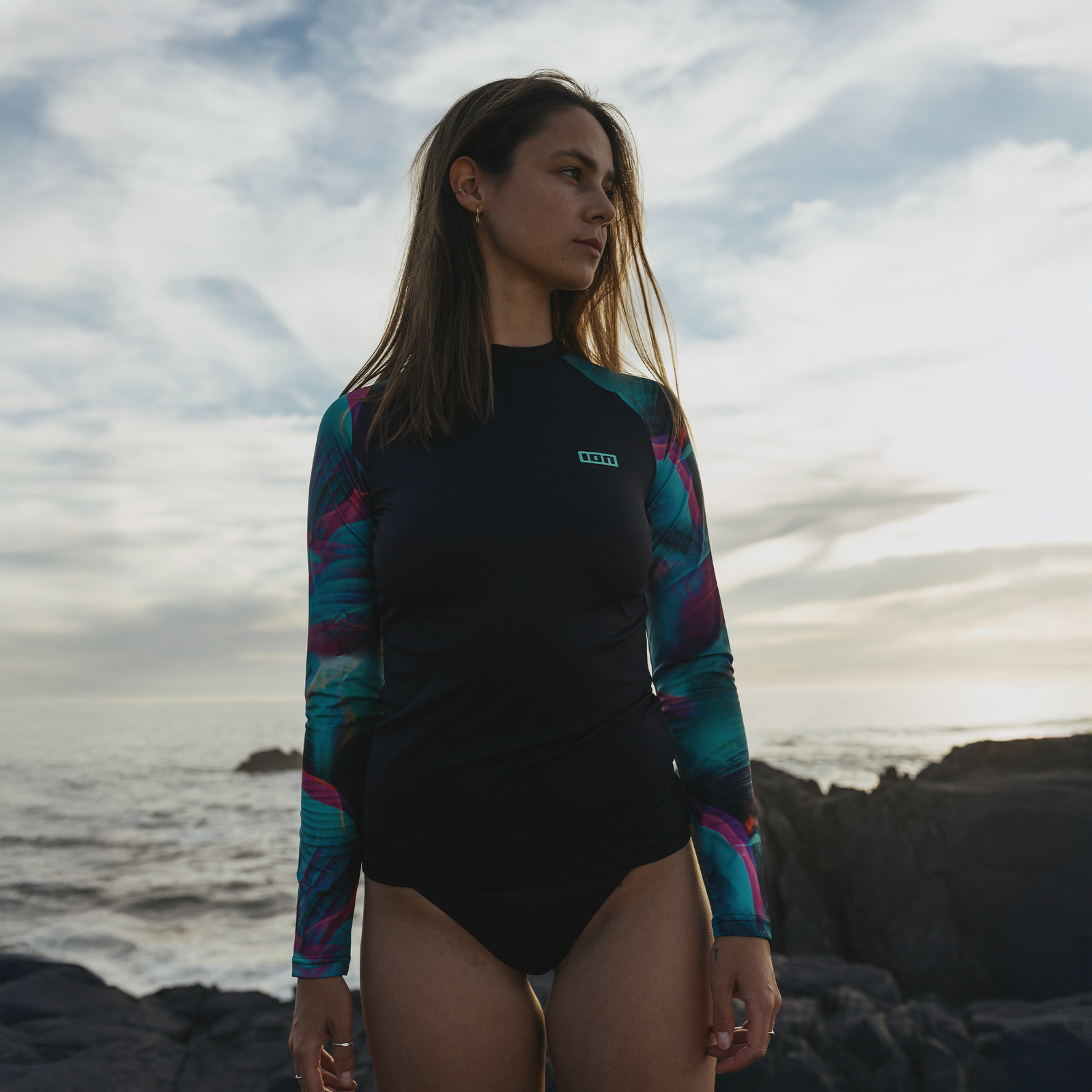 ION Lizz Langarm-Rashguard Damen in schwarz, türkis und magenta beim Stehen an der Felsenküste