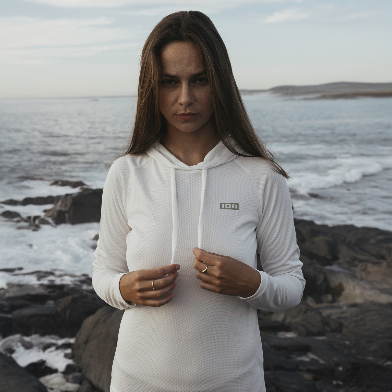 ION Wetshirt Hood LS women's long-sleeve hooded wetshirt in white at a rocky coastline